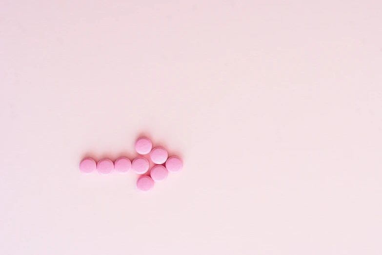 a bunch of pink pills sitting on top of a white surface, by Emma Andijewska, trending on pexels, antipodeans, arrow shaped, cross, minimalist photorealist, construction