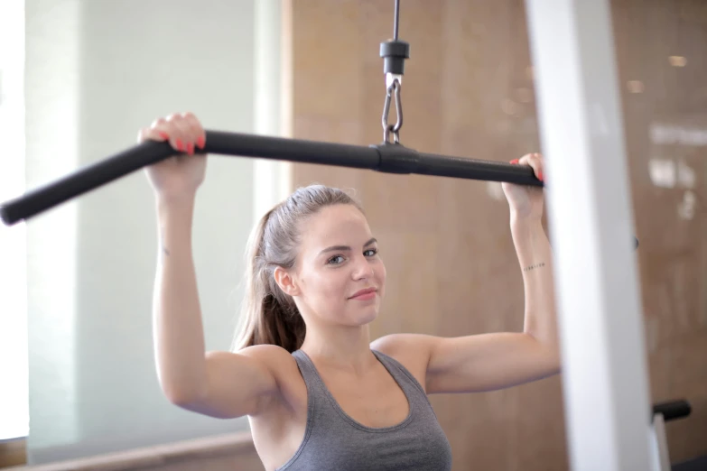 a woman using a pull up bar in a gym, a portrait, by Arabella Rankin, dribble, private press, grey, high-quality photo, blair armitage, slight smirk