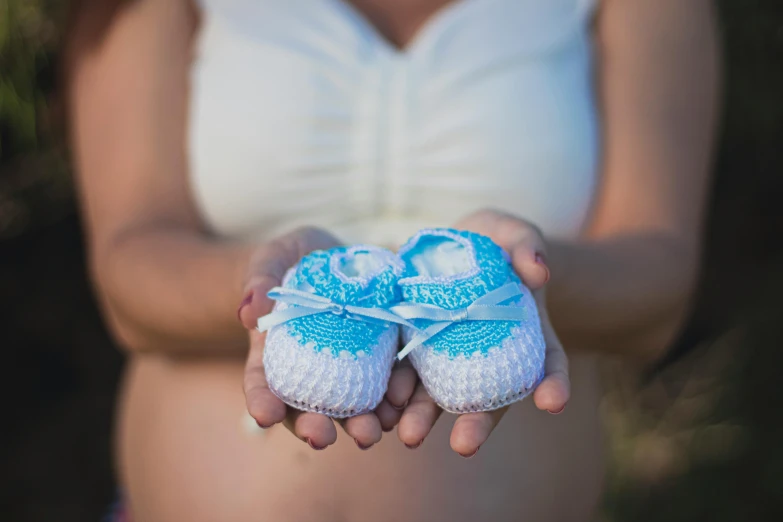 a woman holding a pair of baby shoes in her hands, by David Allan, pexels contest winner, white and blue, avatar image, pregnancy, crochet