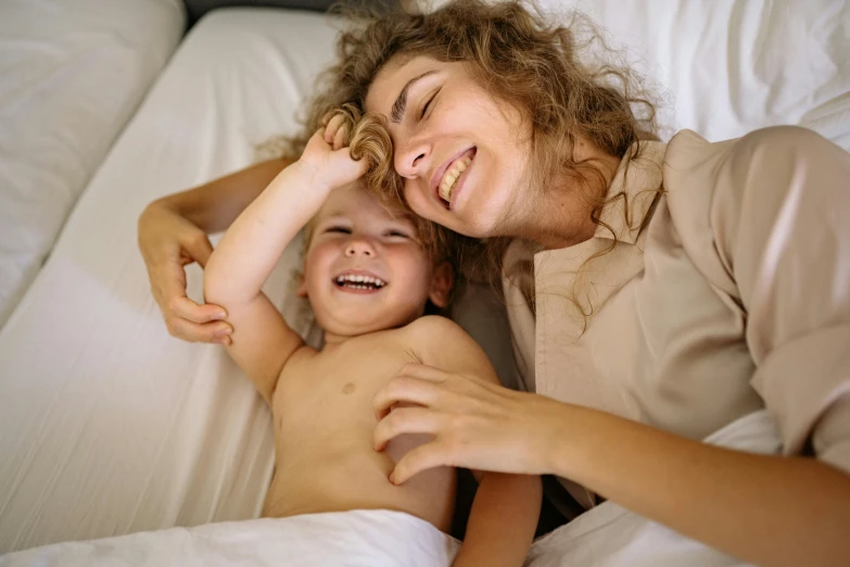 a woman laying on top of a bed next to a child, pexels contest winner, head bent back in laughter, thumbnail, closeup - view, portrait of small