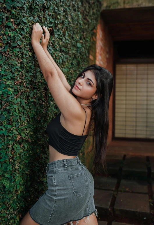 a beautiful young woman leaning against a wall, inspired by Elsa Bleda, pexels contest winner, provocative indian, greenery, doing a sassy pose, black top