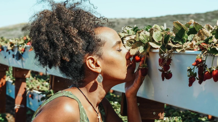 a woman smelling a bunch of strawberries in a garden, trending on unsplash, brown skinned, avatar image, hydroponic farms, laying on roses