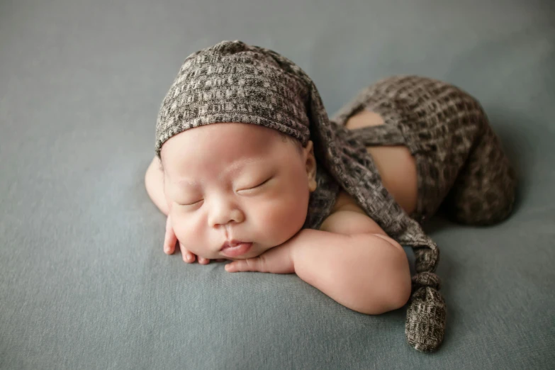 a close up of a baby sleeping on a blanket, inspired by Anne Geddes, shutterstock contest winner, dressed in a gray, small hat, muted browns, thawan duchanee