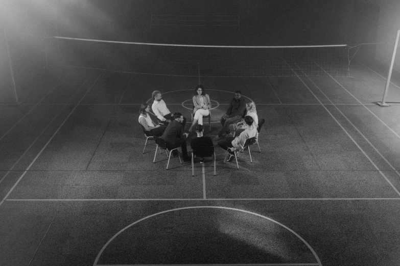 a group of people sitting around a table on a tennis court, a black and white photo, unsplash, surrealism, everything enclosed in a circle, ffffound, taken in the night, 7 0 s cinestill