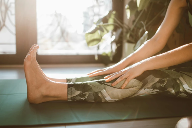 a woman sitting on a yoga mat in front of a window, pexels contest winner, shows a leg, sprawled out, manuka, green legs