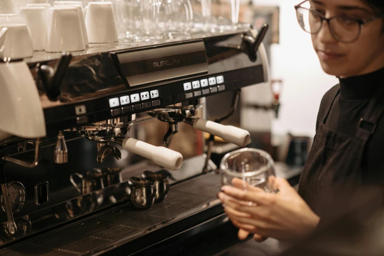 a woman standing in front of a coffee machine, by Nick Fudge, pexels contest winner, lachlan bailey, hands on counter, avatar image