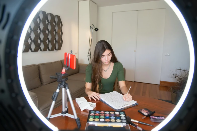 a woman sitting at a table in front of a camera, prismacolor, a glowing halo, studying, youtube thumbnail