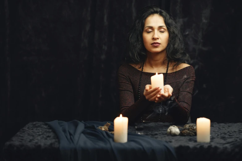 a woman sitting at a table holding a candle, trending on pexels, renaissance, maya ali as a sorcerer, studio photo, holy ceremony, black - haired mage