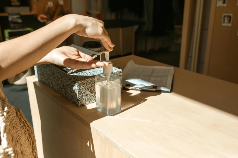a person sitting at a table with a bottle of hand sanitizer, unsplash, sustainable materials, melbourne, dwell, pouring