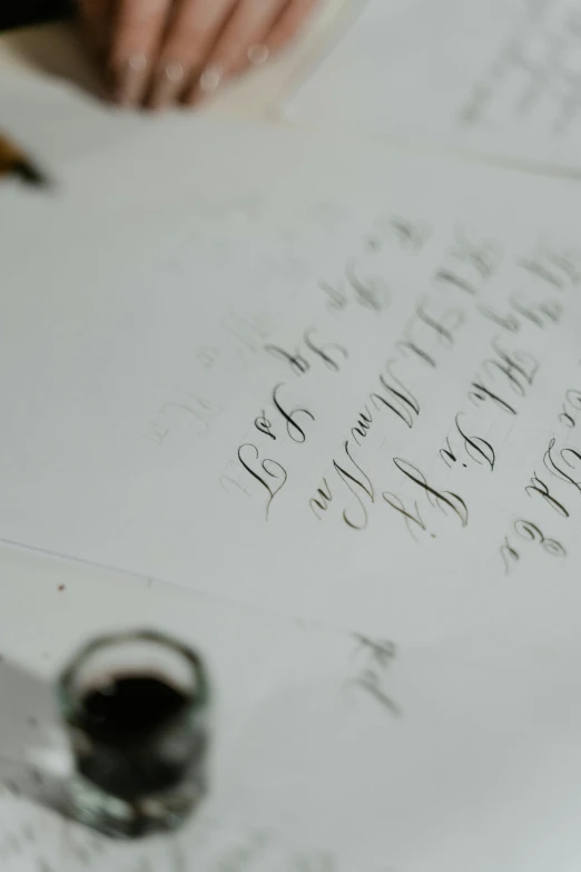 a close up of a person writing on a piece of paper, an album cover, unsplash, letterism, silver，ivory, calligraphy, grey, 1811