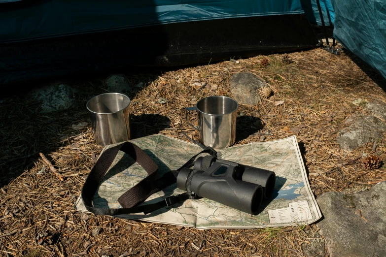 a pair of binoculars sitting on top of a map, barrel fires and tents, soup, photograph, grey