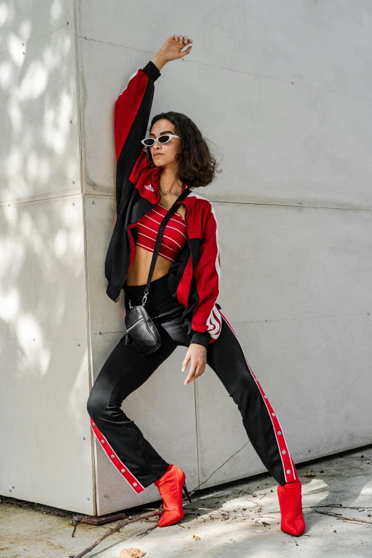 a woman in a red and black outfit leaning against a wall, by Nina Hamnett, trending on pexels, wearing a track suit, bra and shorts streetwear, bella poarch, split near the left