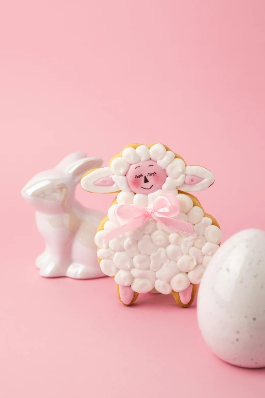 a cookie sitting next to an egg on a pink surface, folk art, lamb and goat fused as one, full product shot, detailed product image, full face shot