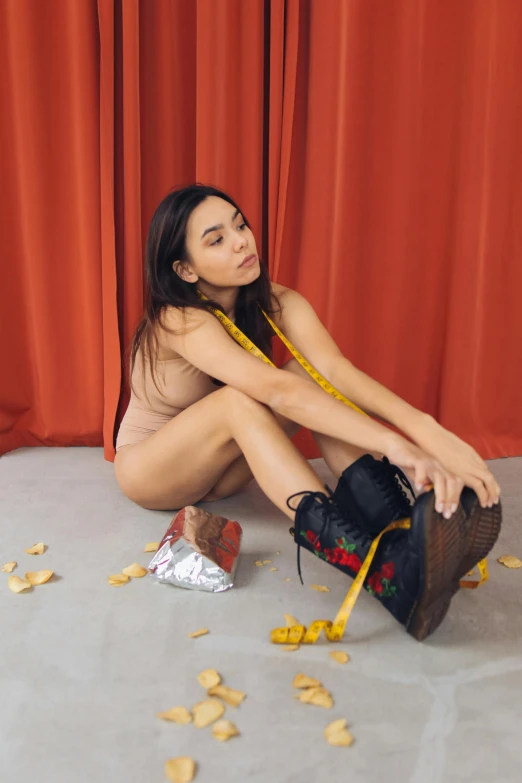 a woman sitting on the floor in front of a red curtain, inspired by Sarah Lucas, trending on pexels, conceptual art, :: madison beer, wearing boots, plastic skin, kiko mizuhara