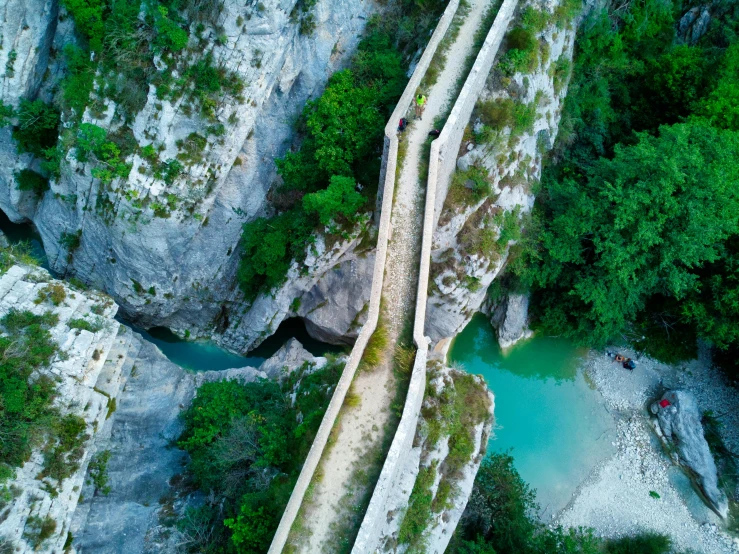 an aerial view of a bridge over a river, by Jean-Yves Couliou, les nabis, rock walls, cyan, hiking trail, conde nast traveler photo