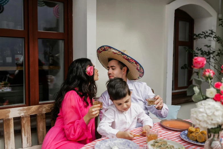 a man and woman sitting at a table with a child, pexels contest winner, sombrero, drinking, portrait image, square