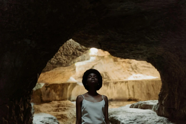 a woman in a white dress standing in a cave, inspired by Gordon Parks, unsplash contest winner, afrofuturism, still from a wes anderson film, black teenage girl, ignant, young girl