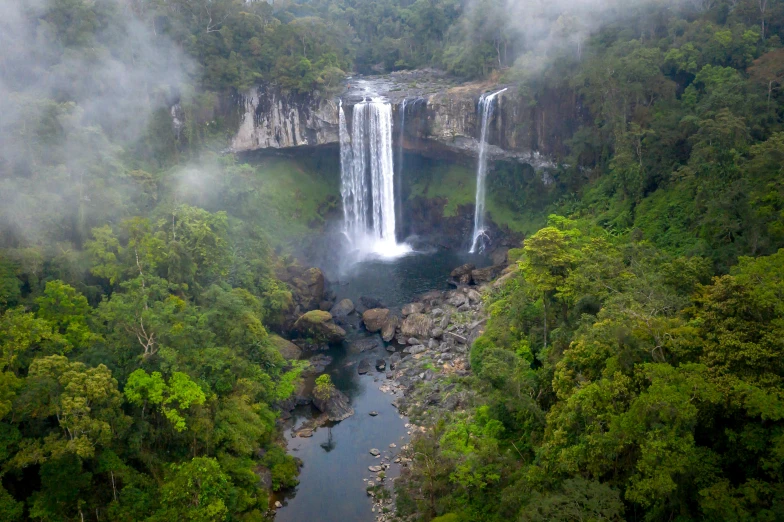 a waterfall in the middle of a lush green forest, rainbow river waterfall, lisa brawn, epic land formations, as seen from the canopy