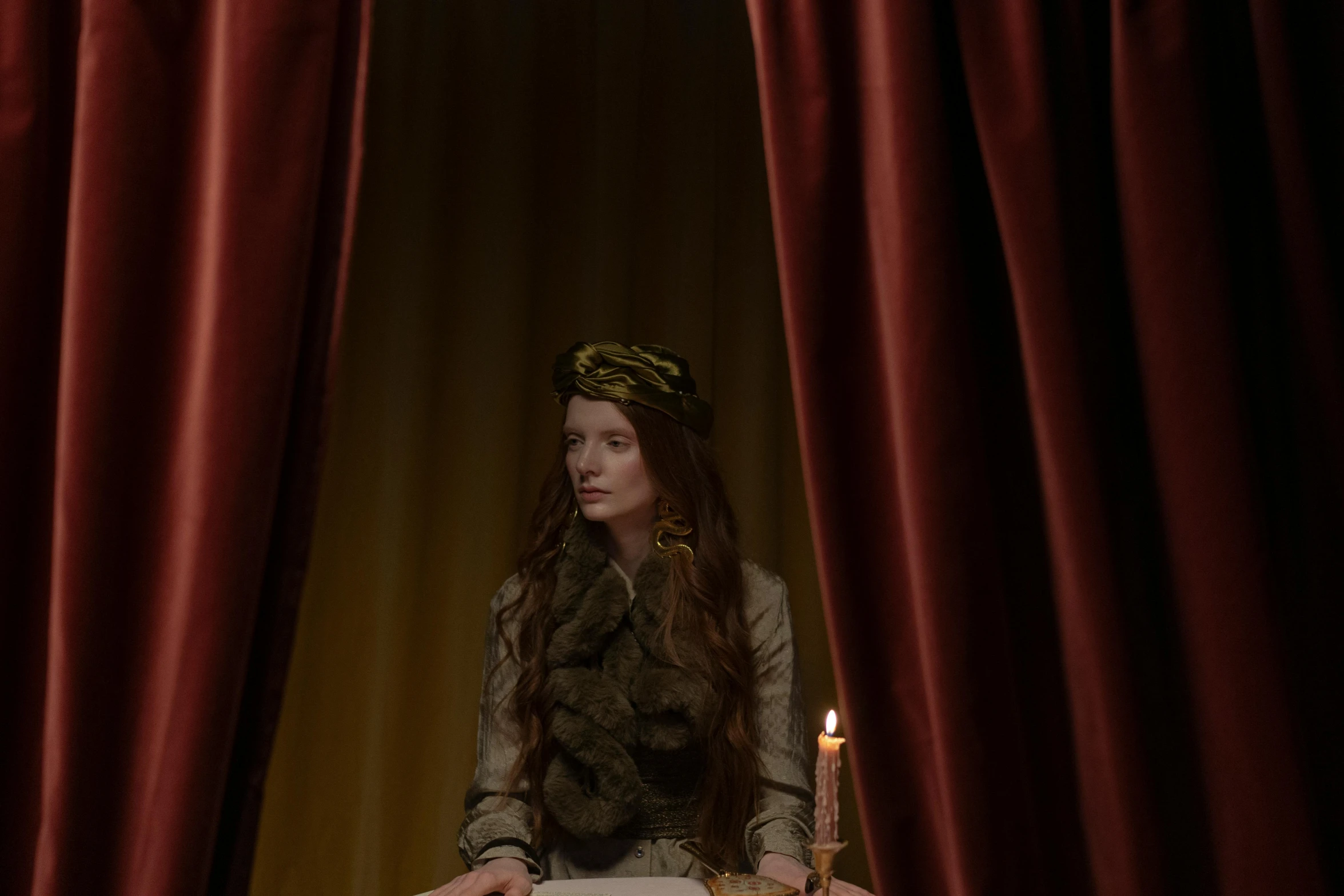 a woman sitting at a table with a book and a candle, inspired by Edwin Austin Abbey, renaissance, anya taylor - joy and emma stone, behind red curtains, ( ( theatrical ) ), karen gillan