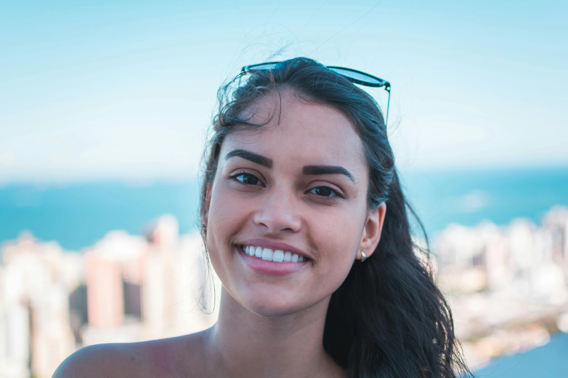 a woman smiling at the camera with a city in the background, by Amelia Peláez, pexels contest winner, tanned skin, halfbody headshot, underbite, avatar image