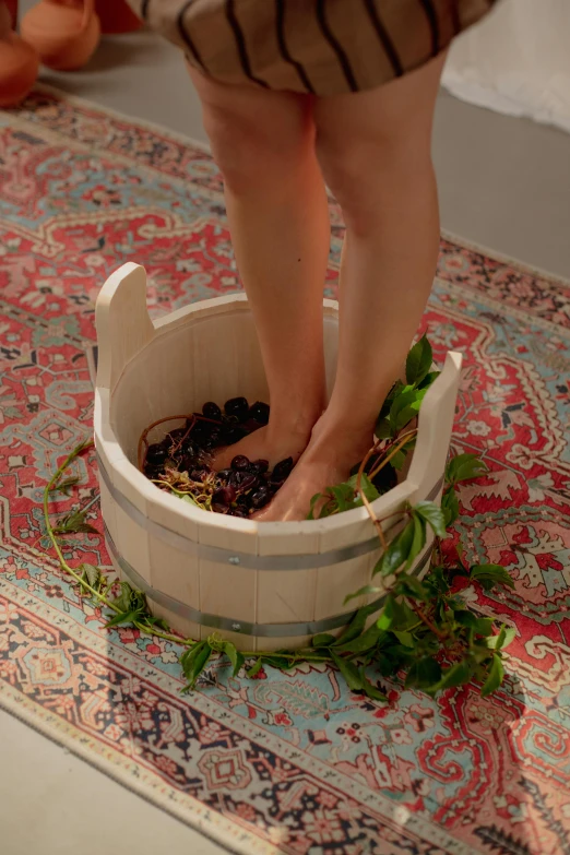 a person standing over a bowl of food on a rug, bare foot, wild berry vines, bathtub, barrels