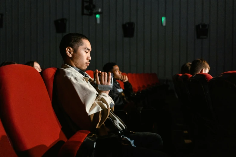 a man sitting on a red chair in a movie theater, inspired by Fei Danxu, unsplash, visual art, praying posture, ruan jia and fenghua zhong, 4k movie still, ignant