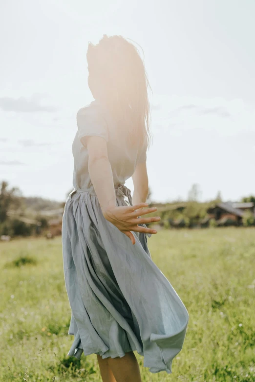 a woman standing on top of a lush green field, soft grey and blue natural light, wearing a skirt, portrait featured on unsplash, walking away