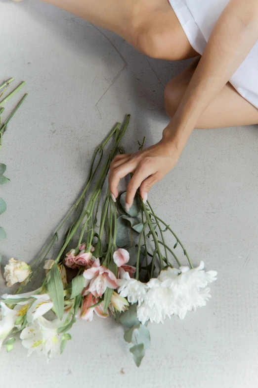 a woman sitting on the floor holding a bunch of flowers, inspired by François Boquet, trending on unsplash, low detail, laying down, stems, hand on table