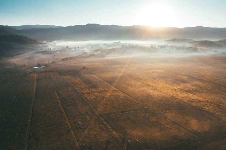 a hot air balloon flying over a field on a sunny day, by Sebastian Spreng, unsplash contest winner, land art, mist in valley, drone view of a city, sun puddle, lachlan bailey