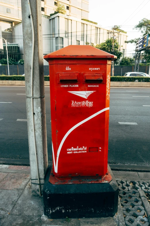 a red mail box sitting on the side of a road, an album cover, unsplash, bangkok townsquare, low quality photo, postage, square