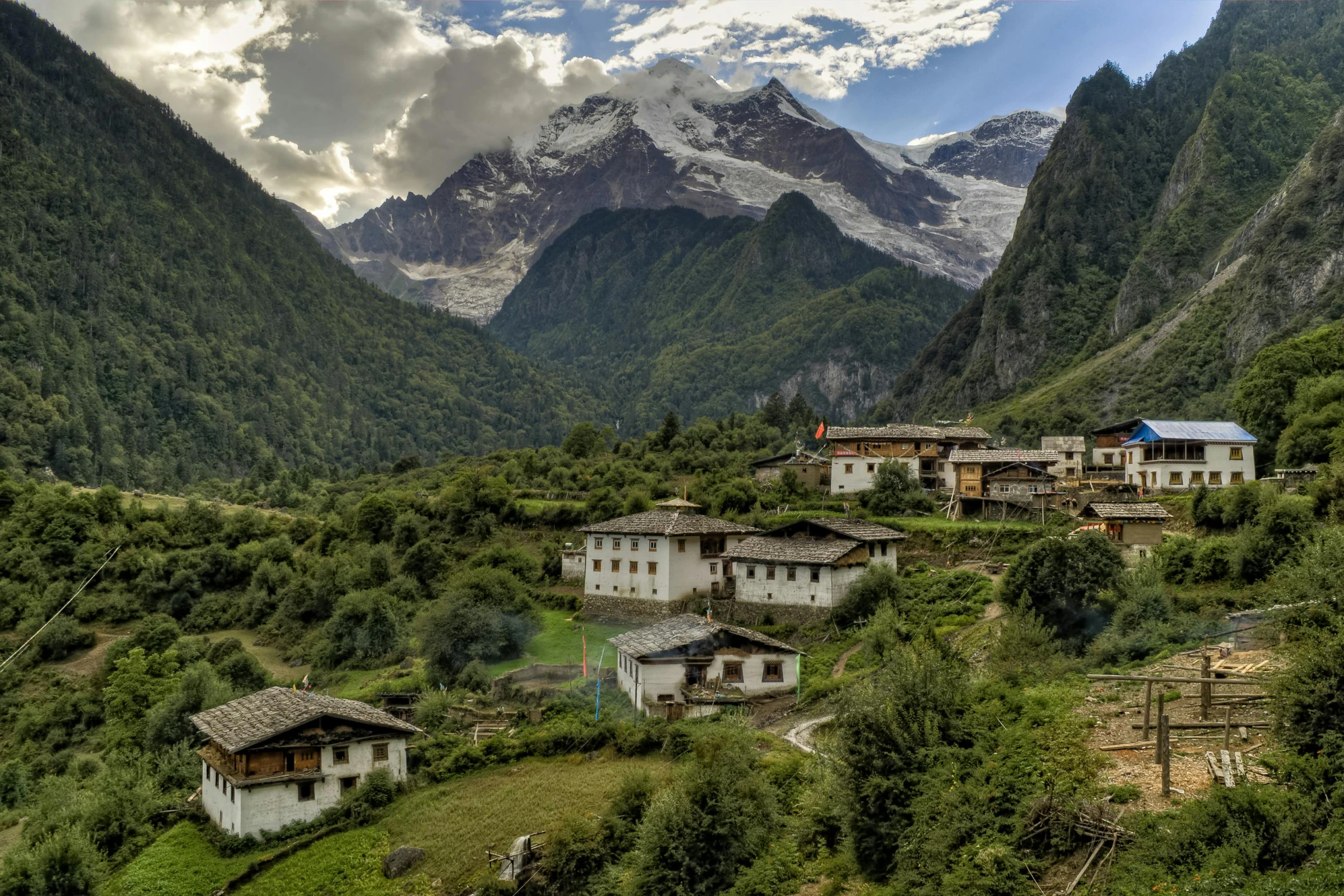 a group of houses sitting on top of a lush green hillside, by Peter Churcher, pexels contest winner, hurufiyya, sichuan, avatar image, icy mountains in the background, conde nast traveler photo