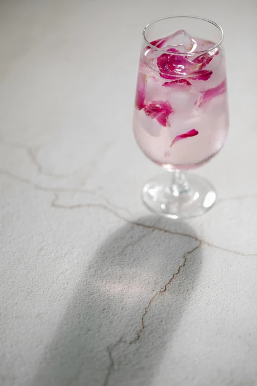 a glass filled with pink liquid sitting on top of a counter, inspired by Antonio Rotta, cracked earth, detail shot, opal petals, white concrete