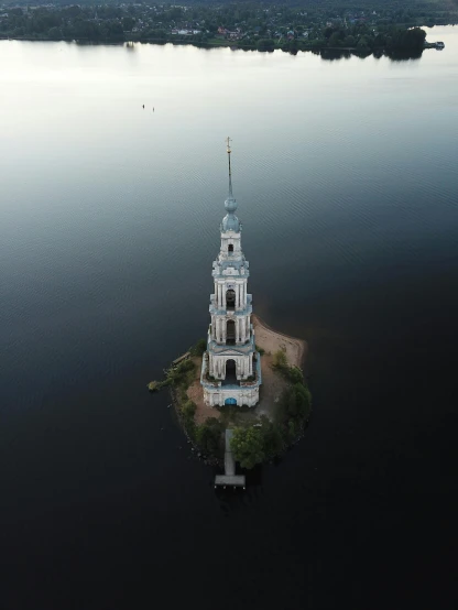 a church sits on an island in the middle of a lake, by Alexey Venetsianov, pexels contest winner, gigantic tower, aerial, high res 8k, grey