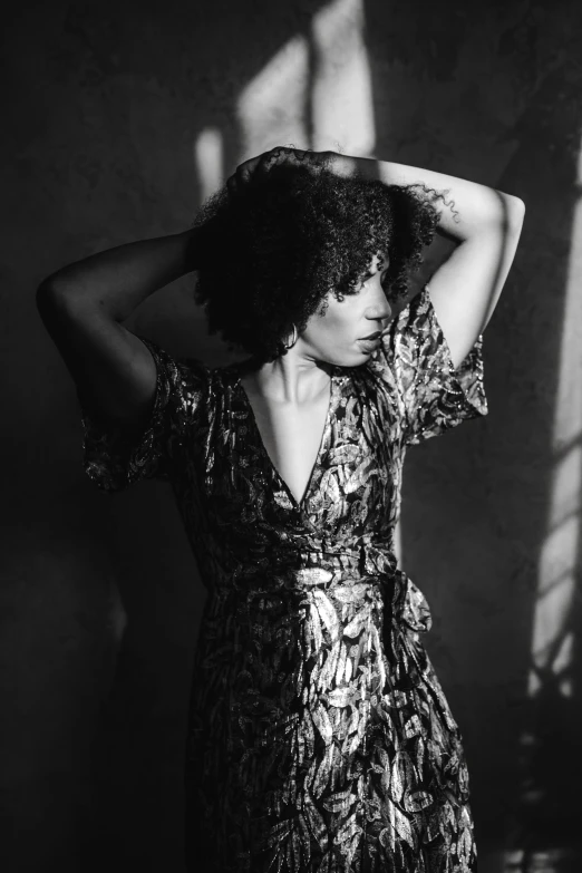 a black and white photo of a woman in a dress, by Winona Nelson, pexels contest winner, curly afro, warm lighting with cool shadows, her hand is on her waist, her hair is tied above her head