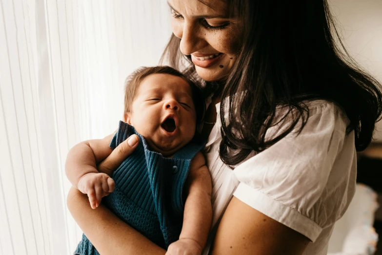 a woman holding a baby in her arms, pexels contest winner, bowater charlie and brom gerald, winking, 1450, lachlan bailey