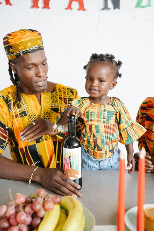 a woman and two children sitting at a table with a bottle of wine, an album cover, by Ingrida Kadaka, pexels contest winner, wearing an african dress, dad energy, at a birthday party, a colorful