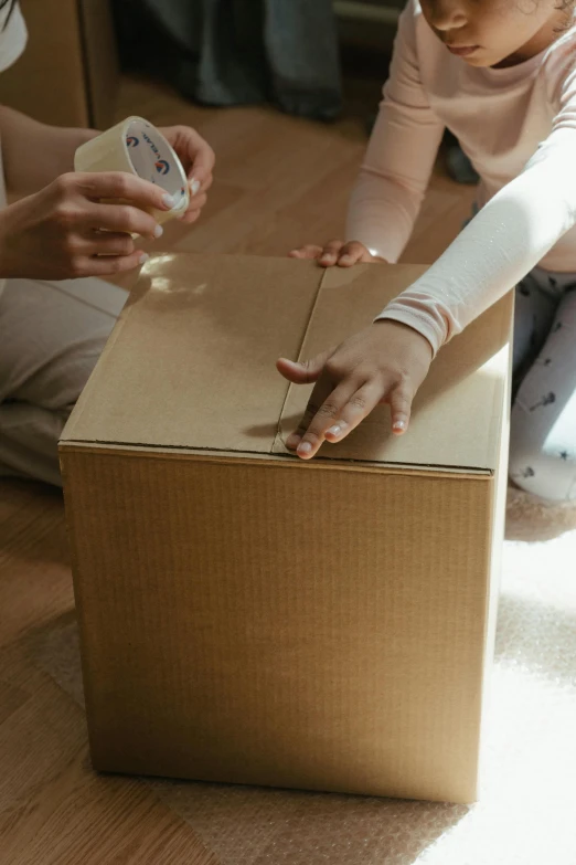 a little girl sitting on the floor next to a cardboard box, by Andries Stock, pexels contest winner, tactile buttons and lights, repairing the other one, pregnant, close together