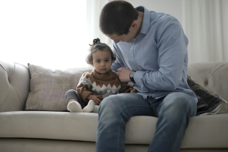 a man sitting on a couch next to a little girl, pexels, hurufiyya, heartbroken, te pae, holding an epée, grey