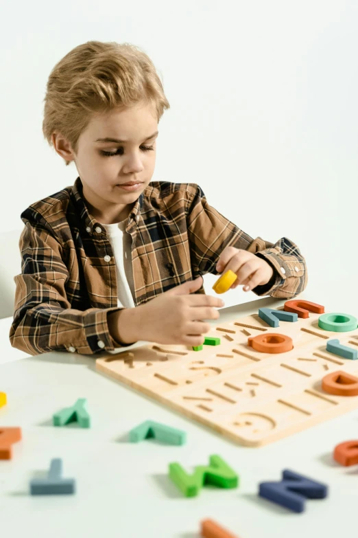 a little boy that is sitting at a table, a jigsaw puzzle, inspired by Frederick Hammersley, trending on pexels, geometric wood carvings, uppercase letter, product image, pastel'