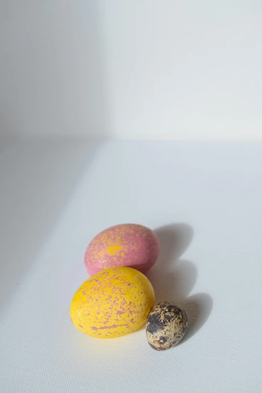 three eggs sitting next to each other on a table, a picture, by Jan Tengnagel, yellow purple, covered with pink marzipan, taken with sony alpha 9, speckled