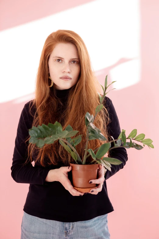 a woman holding a potted plant in front of a pink wall, with long red hair, profile image, promotional image, houseplants
