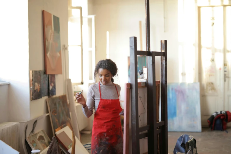 a woman in an artist's studio working on a painting, pexels contest winner, arbeitsrat für kunst, aida muluneh, artist wearing overalls, canvas coated with red paint, portrait of tall