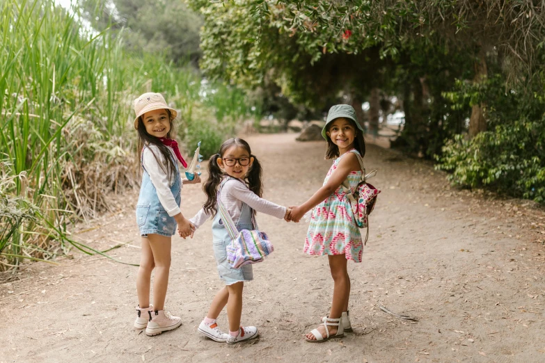 three little girls holding hands on a dirt road, pexels contest winner, standing in a botanical garden, with a backpack, diverse outfits, having a picnic