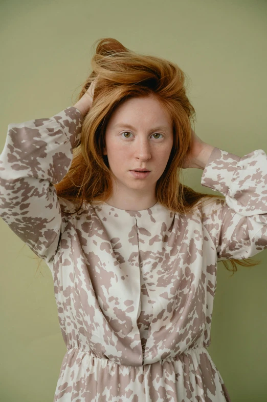 a woman standing in front of a green wall, an album cover, by Annabel Eyres, trending on pexels, renaissance, ginger hair with freckles, on a gray background, patterned clothing, on a pale background