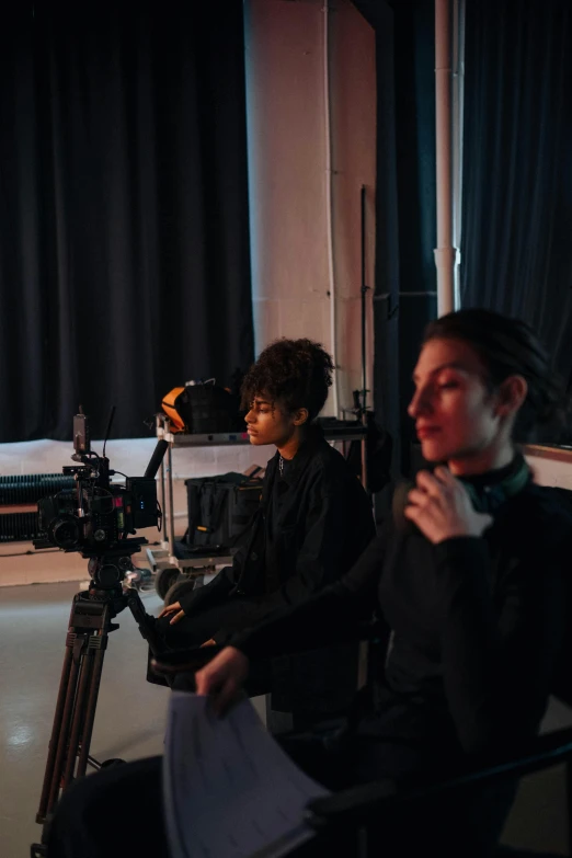 a couple of people sitting in front of a camera, by Jacob Toorenvliet, trending on pexels, video art, theatre equipment, girl in studio, ashteroth, looking back at the camera