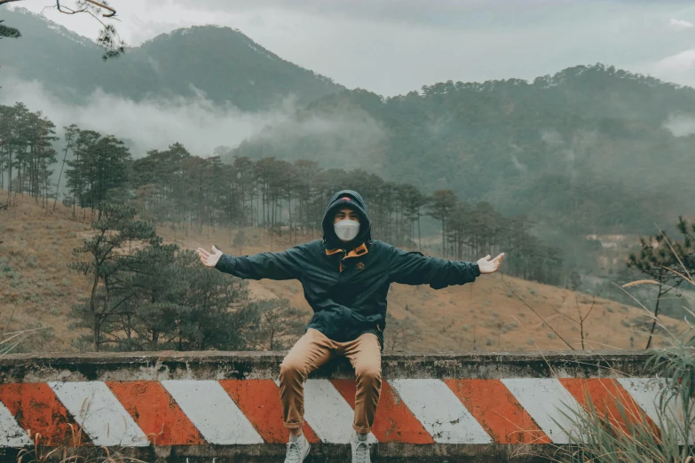a man sitting on top of a red and white barricade, a picture, pexels contest winner, graffiti, solo hiking in mountains trees, wearing mask, avatar image, cloudy air