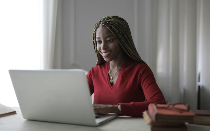 a woman sitting in front of a laptop computer, pexels contest winner, maroon and white, black girl, wearing red, student