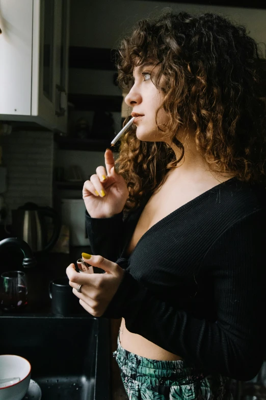 a woman smoking a cigarette in a kitchen, inspired by Elsa Bleda, pexels contest winner, renaissance, brown curly hair, mid 2 0's female, black top, nug pic