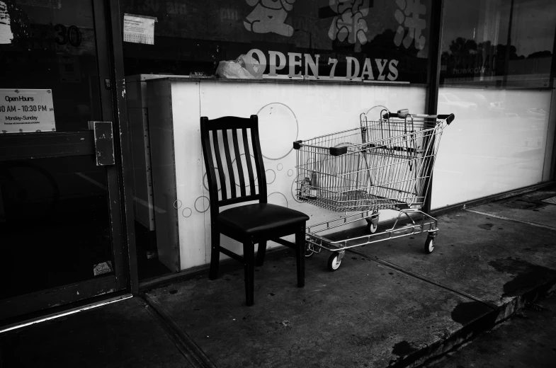 a black and white photo of a shopping cart and a chair, a black and white photo, by Josh Bayer, seven, old shops, ossdraws, hunger