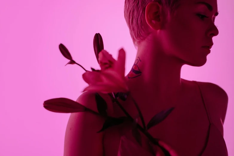 a woman holding a flower in front of a pink background, an album cover, inspired by Elsa Bleda, trending on pexels, detailed neon tattoos, purple ambient light, view from the side, bisexual lighting